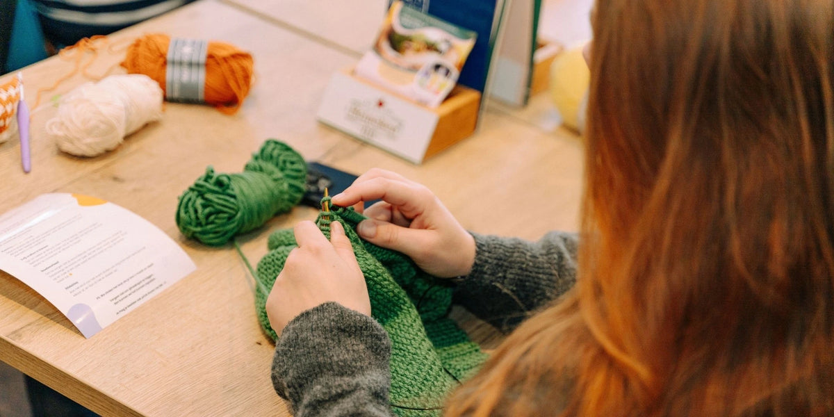 Vrouw met rode haren haakt aan groen werk aan tafel met garenbollen.
