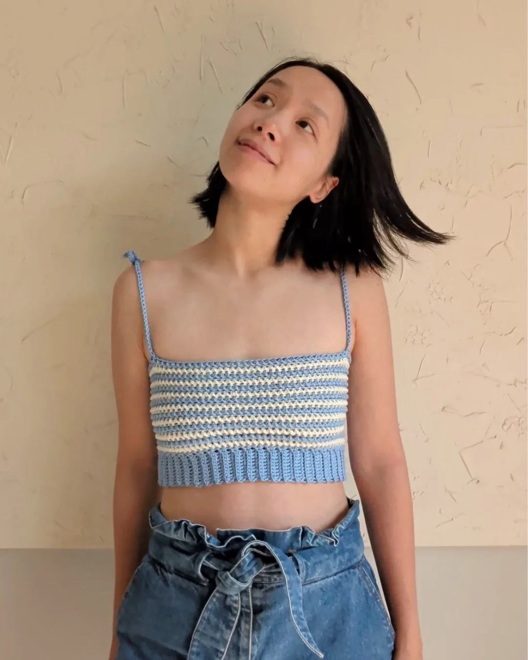 Vrouw draagt gehaakte Striped Top in blauw en ecru, gecombineerd met een jeans broek