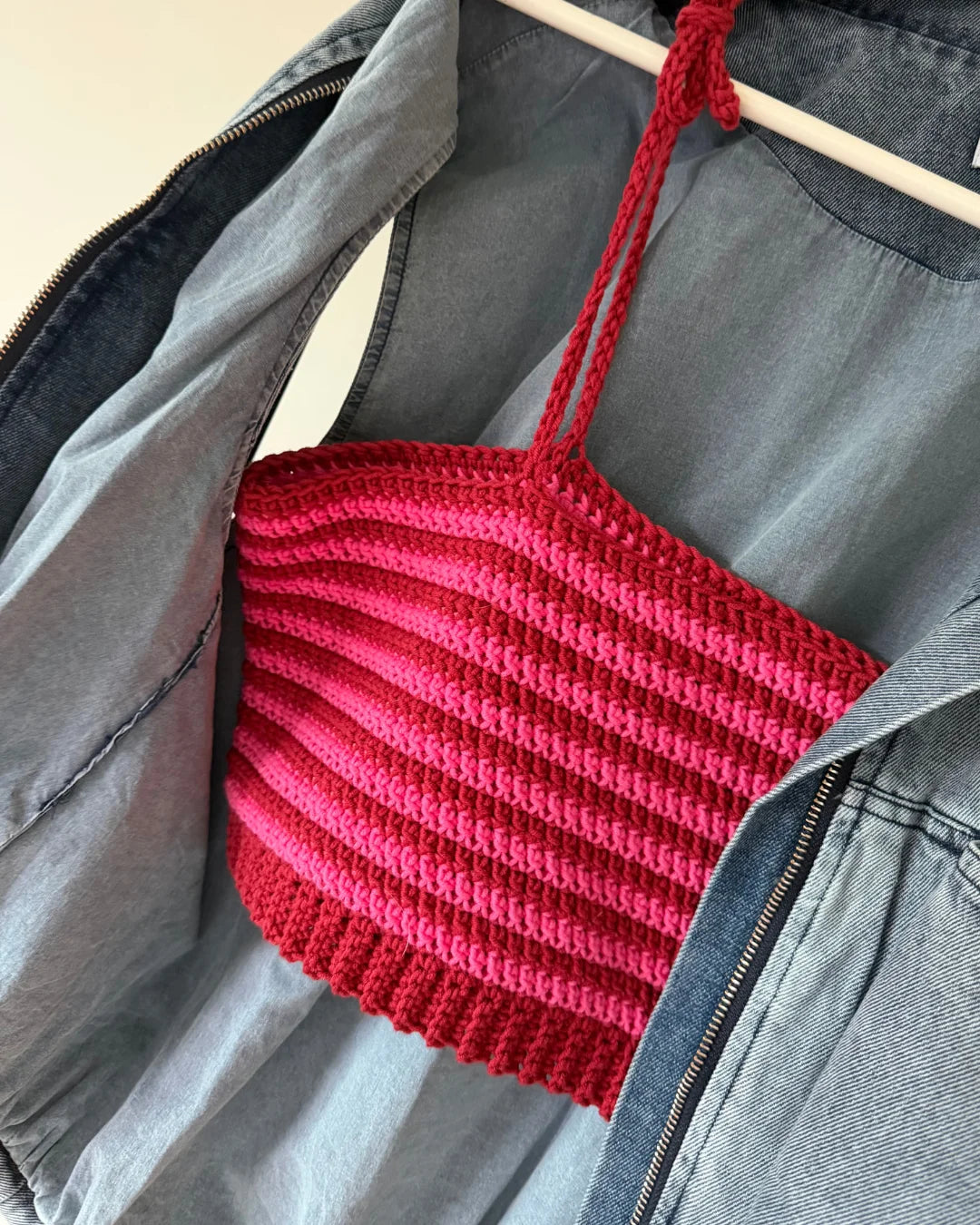 Gehaakte Striped Top in rood en roze op hanger, over spijkerjasje op lichtblauwe achtergrond.