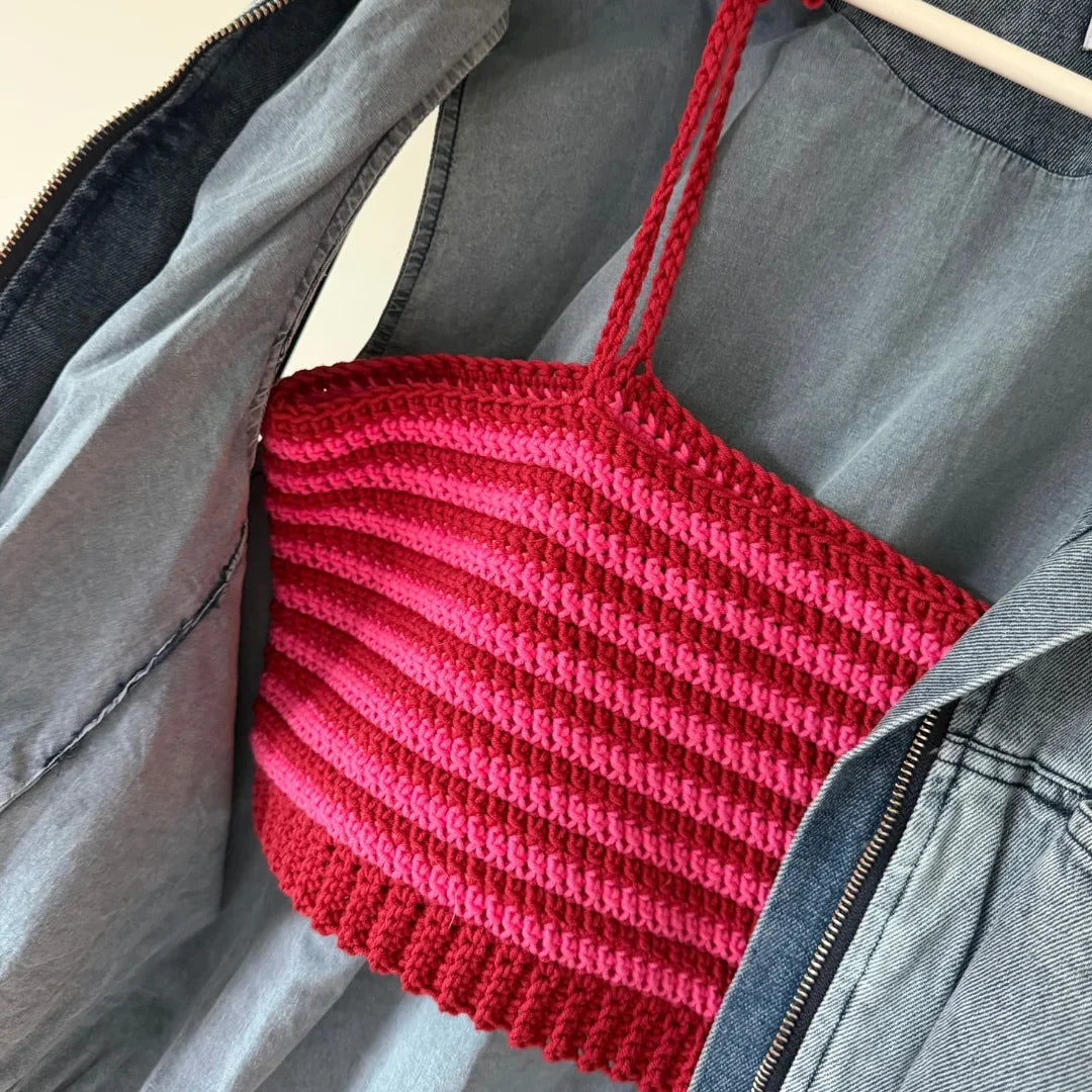 Gehaakte Striped Top in rood en roze op hanger, over spijkerjasje op lichtblauwe achtergrond.