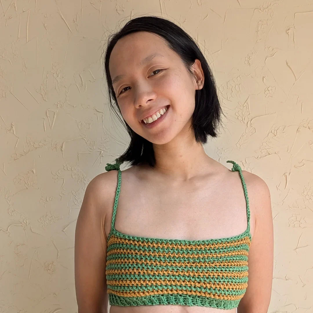 Lachende vrouw draagt gehaakte Striped Top in groen en oker met spaghettibandjes, boven jeans.