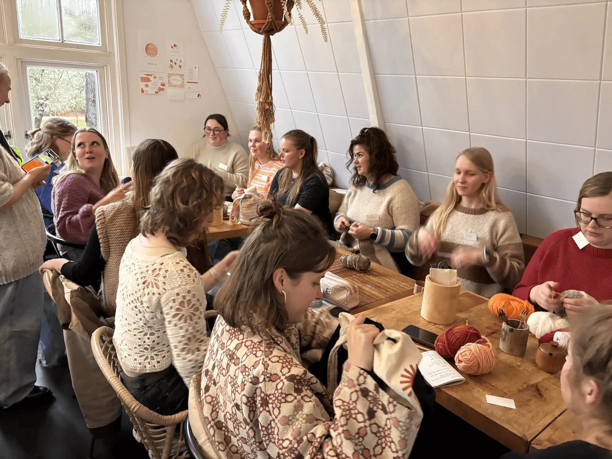 Groep vrouwen haakt samen aan een lange houten tafel met bollen garen in warme kleuren.