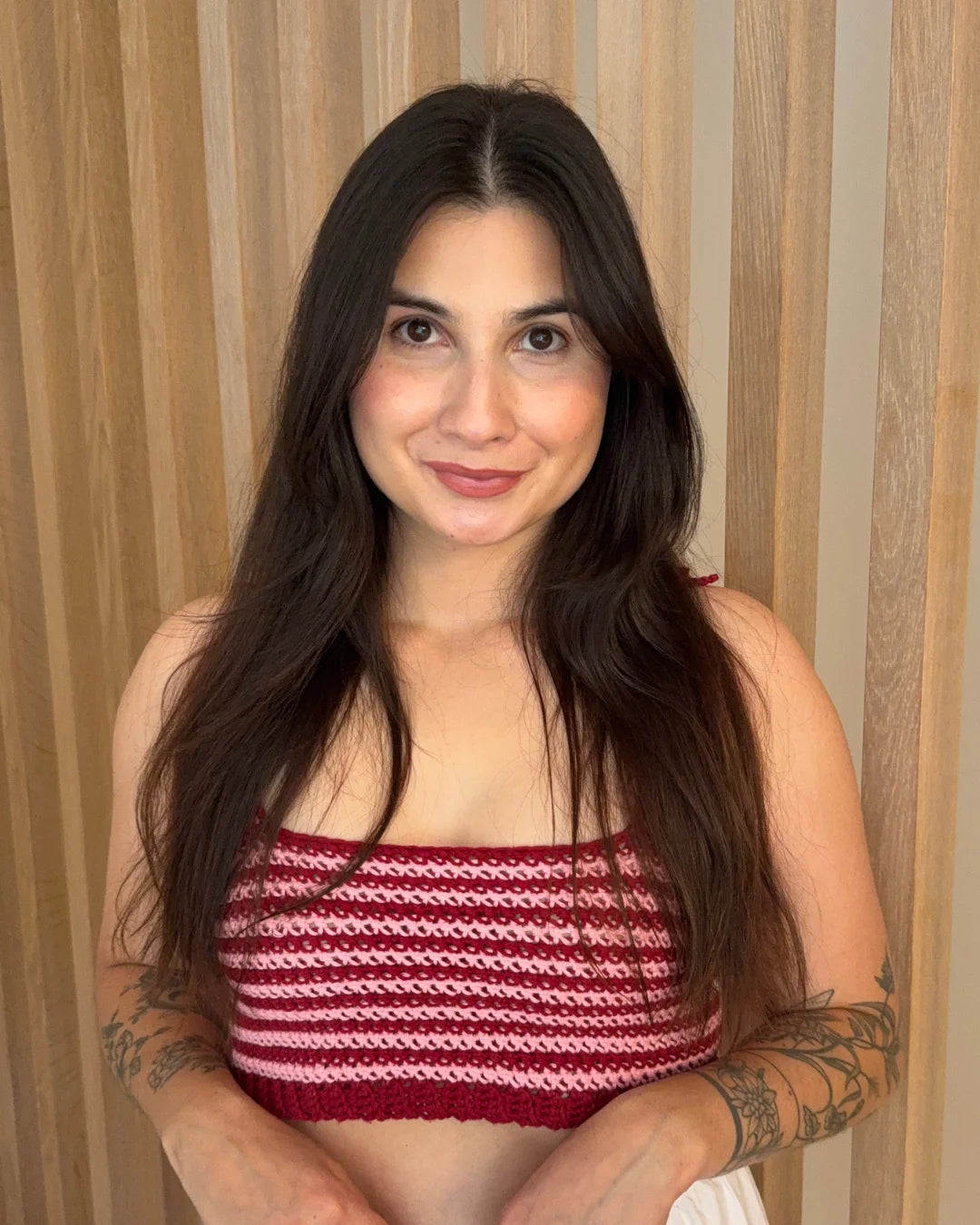Vrouw met lang donker haar draagt de gehaakte Striped Top in rood en roze strepen