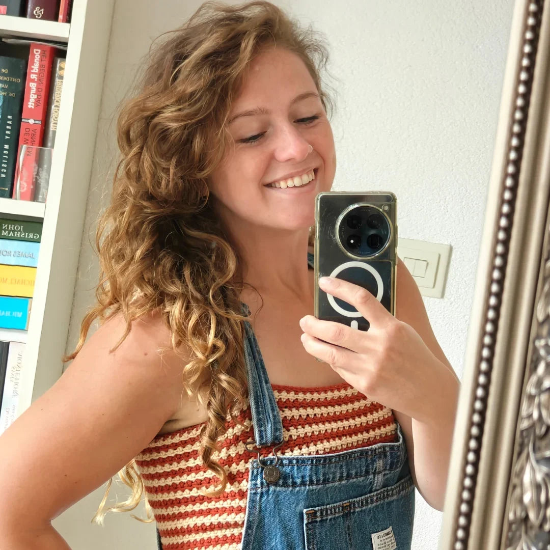 Lachende vrouw maakt spiegelselfie in gehaakte Striped Top met rood-beige strepen onder denim tuinbroek