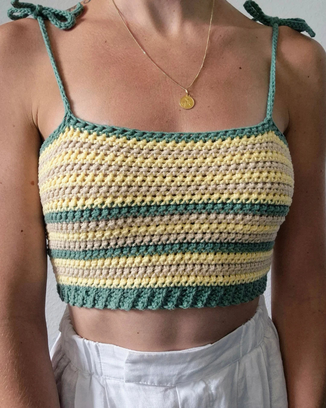 Vrouw draagt gehaakte Striped Top met groene, gele en beige strepen en schouderbandjes met strikjes