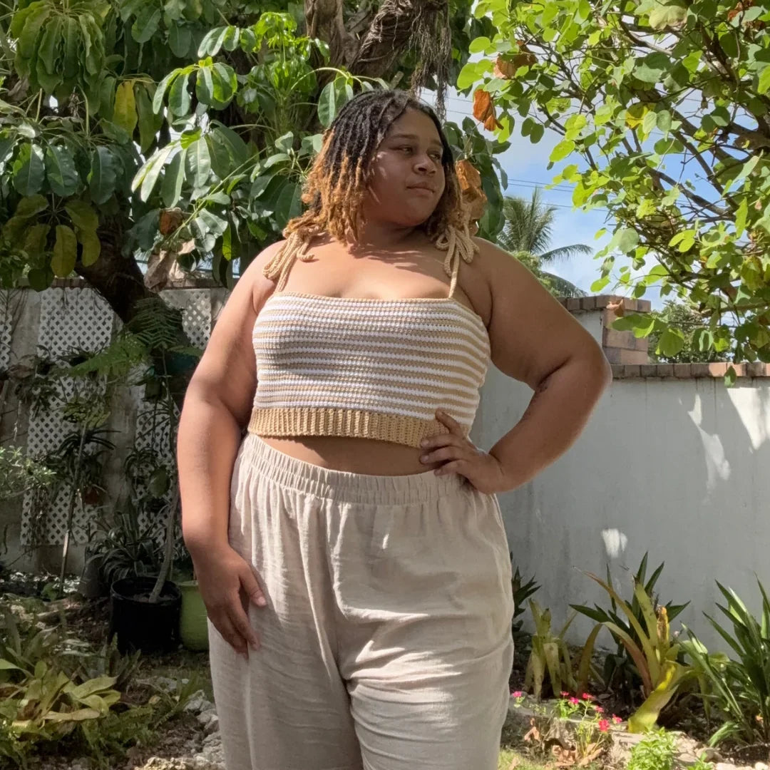 Vrouw draagt gehaakte Striped Top in oker en wit met beige broek in zonnige tuin